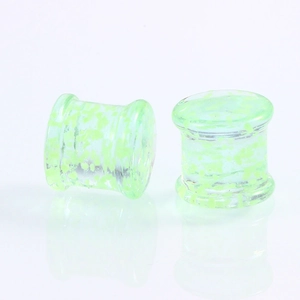 Nahaufnahme von Double Flare Glas-Ohrplugs mit grünen Leuchtflecken und transparenter Optik