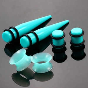 Detailliertes Set aus türkisfarbenen Acryl-Ohrdehnersets und Plugs auf dunklem Spiegel