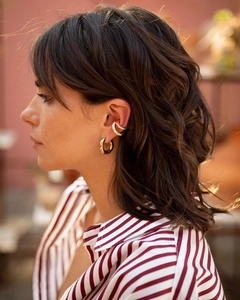 Primer plano de aros dorados y ear cuffs minimalistas en una modelo femenina