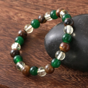 Tiger eye and green crystal beaded bracelet displayed on a pebble over a wooden surface
