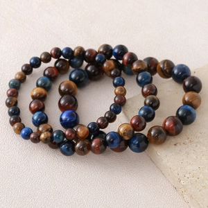 Three natural tiger eye stone beaded bracelets in blue, red, and gold on stone base