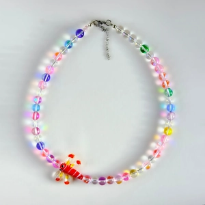 Détail macro d'un collier de perles colorées avec un pendentif libellule rouge sur blanc