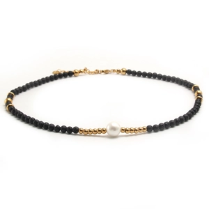Minimalist necklace with black lava stone, metallic gold beads, and a central white pearl