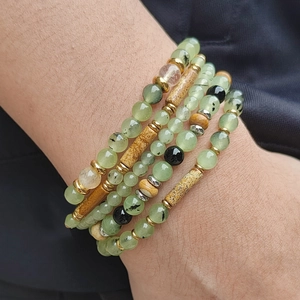 Stacked prehnite and wooden cylinder bead bracelets on a female wrist over black cloth