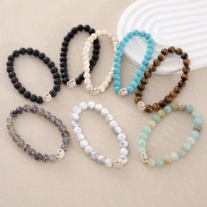 Set of 8mm natural stone beaded bracelets with skull charms on a textured sandy background