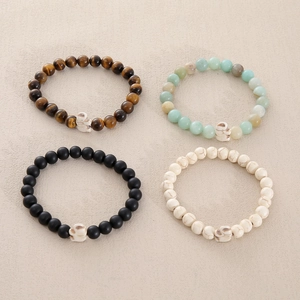 Detail view of four 8mm natural stone beaded bracelets with skull charms in various colors