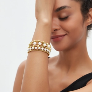 Detail van gelaagde armband met 18K vergulde kralen en elegante witte parels om de pols
