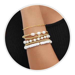 Detail of layered gold beaded and baroque pearl elastic bracelets on woman wrist