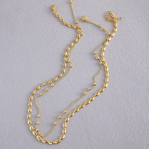 Detail van gouden gelaagde ketting met ovale koffieboonkraaltjes en een fijne kralenketting