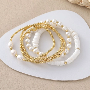 Detail of four-piece beaded bracelet set with baroque pearls and gold beads on white leather
