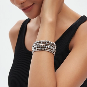 Layered silver metal bead bracelet set for women worn by a model in a minimalist style