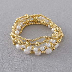 Detailweergave van gelaagde 18K vergulde kralenarmbanden met witte imitatieparels