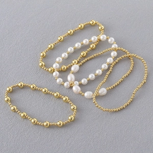 Detail van 5-delige set elastische armbanden met gouden kralen en witte imitatieparels