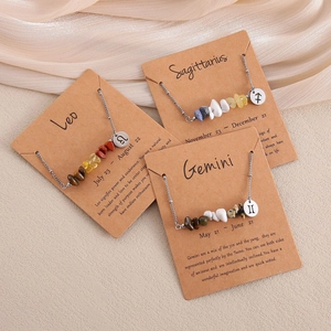 Three zodiac necklaces with natural stones and charms displayed on kraft cards