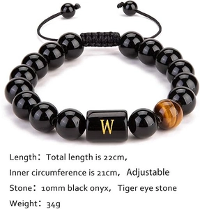 Detalle de pulsera ajustable de ágata negra con piedra ojo de tigre y dije de letra W