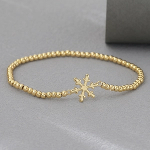 Pulsera de cuentas doradas con un dije de copo de nieve en un estilo festivo de invierno