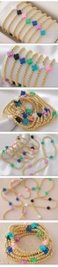Detalle de pulseras elásticas de cuentas doradas con dijes de cruz en varios colores