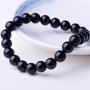 Polished natural black obsidian beaded bracelet for men on a white ceramic plate