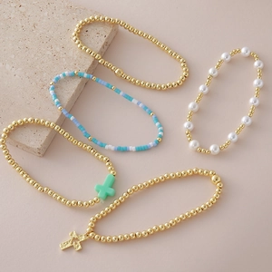 Lot de cinq bracelets perlés dorés avec perles et pendentif croix sur fond de pierre