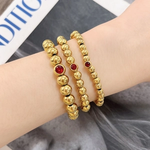 Ensemble de trois bracelets à billes dorées avec pierres de zircon rouges porté par un mannequin