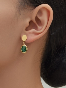 Detailed close-up of gold-plated earrings with faceted dark green glass stone drop