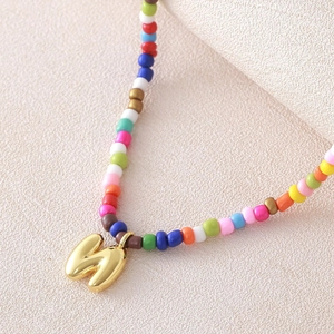 Macro dettaglio della collana di perline colorate con ciondolo a bolla lettera M dorato