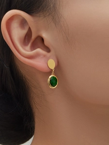 Detail shot of a model wearing gold earrings with faceted oval green glass stone pendants