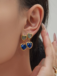 Nahaufnahme der doppelten Herzohrringe mit hellgrünen und blauen Edelsteinen in Gold