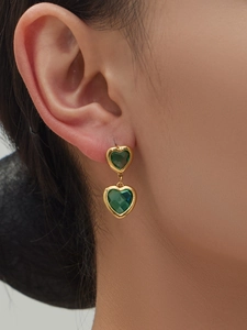 Detail von grünen Herz-Glasohrringen mit Goldmetallrahmen, getragen von einem Modell