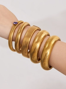 Détail de cinq bracelets tubogas superposés plaqués or 18 carats avec une pierre violette