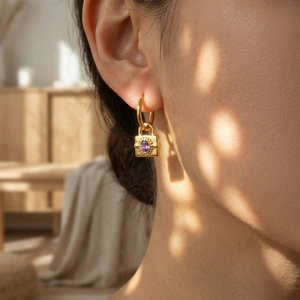 Boucles d'oreilles cadenas dorées avec zircon violet sur un mannequin élégant