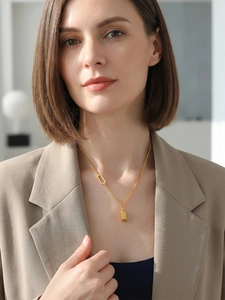Close-up of a gold bar pendant necklace with unique link chain on a beige suit