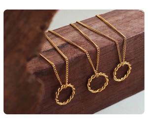 Detail of three golden twisted hoop pendant necklaces on dark wood blocks