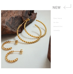 Detailed view of gold twisted metal hoop earring set on minimalist dark wood display