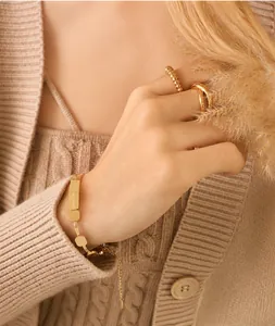 Close-up of a gold engraved bracelet and twisted rings on a model with knitwear
