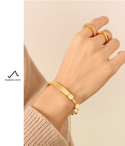 Detail of gold stainless steel bracelet and rings set on model with brand engraving