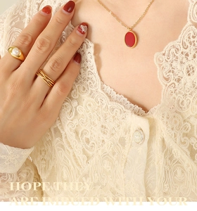 Close-up of golden necklace with red pendant and pearl ring set on lace fabric