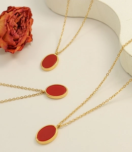 Close-up of golden necklace with red oval pendant set against red dried roses