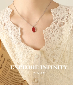 Close-up of a silver chain necklace with an elegant red oval acrylic pendant on lace