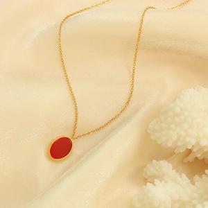 Minimalist gold necklace featuring an oval red acrylic pendant on elegant silk background