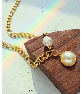 Detail of 18k gold chain necklace with baroque and round pearls on a wooden block