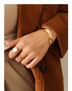 Detail of minimalist gold-plated crossover cuff and shell ring set on model