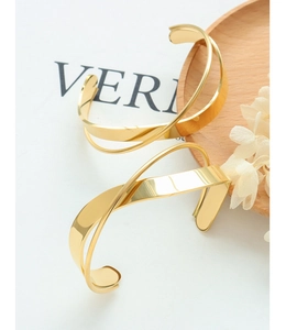 Close-up of polished gold-plated stainless steel criss-cross open bracelets on a wooden tray