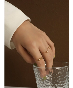 Gros plan de bagues chaînettes à perles en or 18k portées en tenant un verre texturé élégant