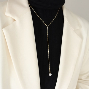 Elegante gouden Y-vormige lange ketting met parelhanger op zwarte coltrui gedragen