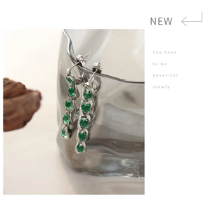 Detail of silver drop earrings featuring emerald cut green zircons in a claw setting
