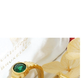 Gros plan d'une bague dorée martelée avec pierre centrale verte sur un support textile