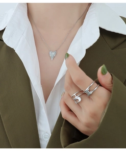 Details von silberner Herzkette und hohlem Ring an Model in grünem Blazer