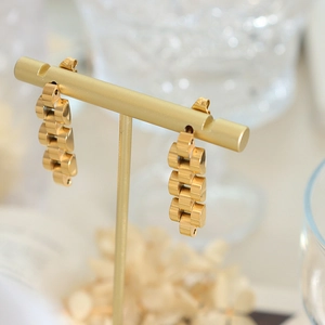 Elegante goldene Uhrenarmband-Ohrringe an einem minimalistischen T-Schmuckständer