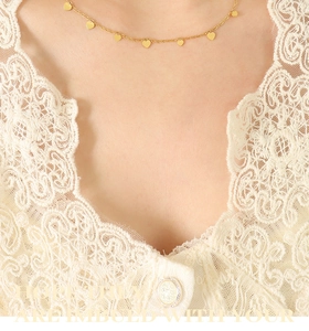 Détail d'un collier ras du cou doré avec pendentifs cœurs porté sur un chemisier en dentelle